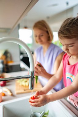 Yetişkinler yemek hazırlarken küçük çocuk sebze yıkıyor..