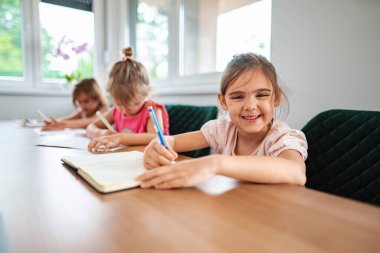 Çocuklar çalışma masasında mutlu bir şekilde yazıp öğreniyorlar..
