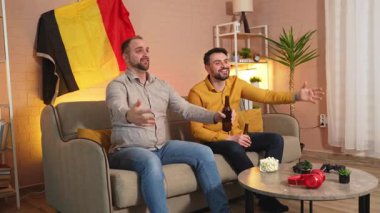 İki arkadaş heyecanlı bir şekilde şık bir yaşam alanında maç izliyor..