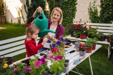 Genç bir kız ve annesi açık havada neşe içinde çiçek yetiştiriyor..