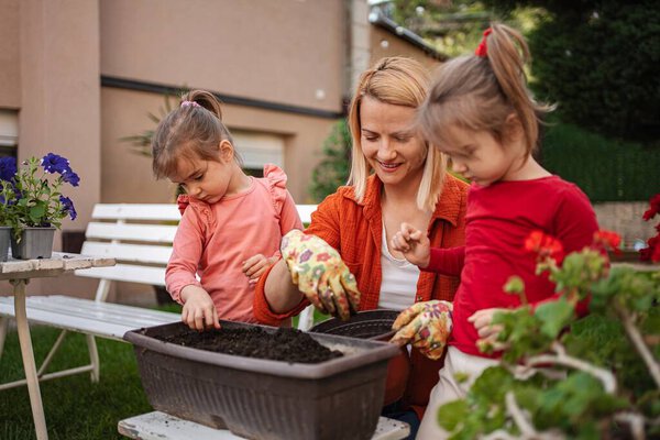 Mother and daughters enjoy planting in a sunny garden.