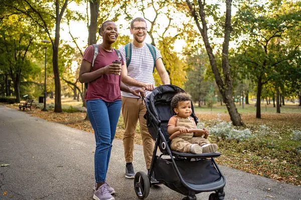Bir çift, sonbahar yapraklarıyla çevrili canlı bir parkta sakin bir yürüyüşün tadını çıkarıyor. Bebek arabasındaki neşeli bebekleri bu güzel günü gözlemler ve sıcak bir aile anı yaratır..