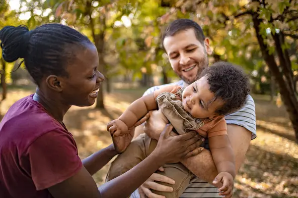 Sonbahar yapraklarıyla dolu sakin bir parkta neşeli bir çift meraklı bebekleriyle neşeli anların tadını çıkarıyor. Sıcak güneş ışığı ağaçların arasından süzülerek rahat bir atmosfer yaratır..