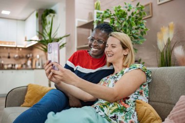 Bitkilerle ve yumuşak dekorlarla dolu sıcak, davetkar bir mekanda, iki arkadaş bir video görüşmesiyle kahkahalarını paylaşıyor, bir neşe ve bağlantı anını yakalıyorlar..