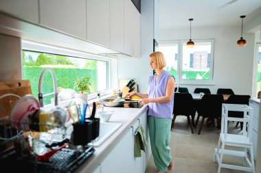 Bir insan güneşli, şık bir mutfakta yemek pişirir..