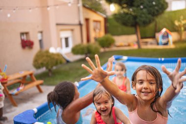 Küçük çocuklar su sıçratıyor ve dışarıda havuzda mutlu bir şekilde oynuyorlar..