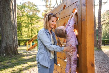 Gülümseyen anne, sevimli kızının oyun parkına çıkmasına yardım ediyor..