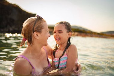 Bir anne ve kızı sıcak okyanus suyunda yürürken kahkahalarını paylaşıyor..