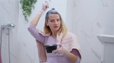 Bir kadın kapalı alanda odaklanmış bir ifadeyi korurken saç boyası sürer..