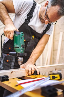 Olgun erkek marangoz, tahtadan bir tahta üzerinde elektrikli tornavida kullanıyor..