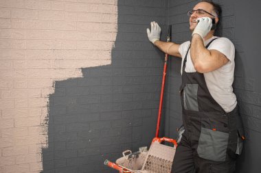 İş elbisesi giymiş gülümseyen bir adam bir eli duvara dayanıyor ve bir telefon görüşmesi yapıyor.