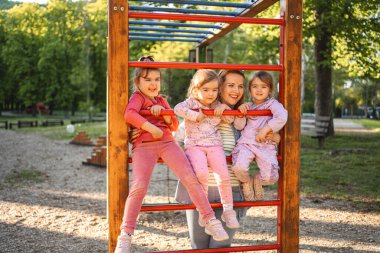 Gülümseyen ve mutlu anne, anaokulu kızı ve ikizleriyle oyun bahçesinde..