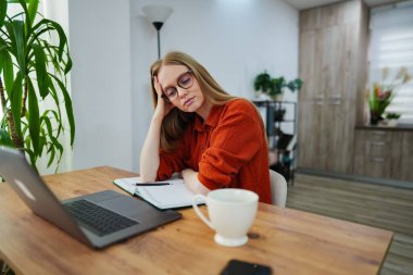 Genç bir kadın, etrafı bitkilerle çevriliyken başını elinin üzerine koyar..