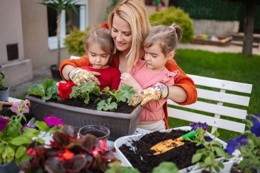 Bir kadın ve iki çocuk saksılara çiçek dikiyor..