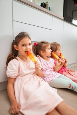 Üç neşeli çocuk dondurulmuş ikramların tadını çıkarıyor, gülümsüyor..