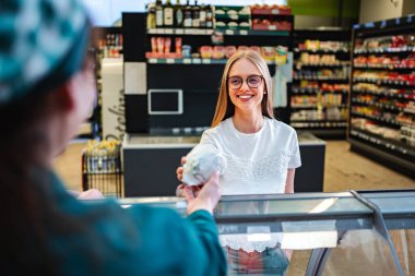 Neşeli bir kadın, canlı bir marketteki bir satıcıdan lezzetli bir aperatif alır. Parlak mağaza, taze ürün ve cazip mallarla dolu hoş bir atmosferi yansıtıyor..