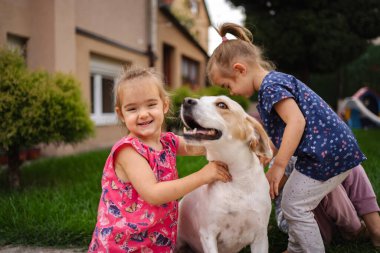 İki genç kız yeşil bir bahçede dost canlısı köpekleriyle mutlu bir şekilde iletişim kuruyor..