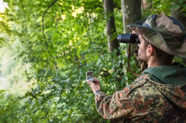 Dürbün ve pusulayı oryantasyon ve keşif için kullanarak sık ormanlarda gezinen asker