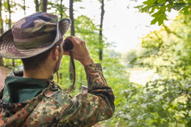 Ormandaki dürbünlerden bakan, kamuflaj takan, etrafı izleyen bir asker.