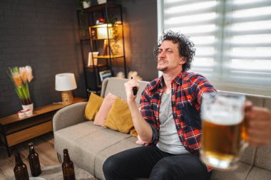 Hüsrana uğramış adam evde televizyon izliyor ve bira içiyor.