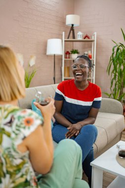 İki arkadaş şık bir oturma odasında otururken birbirlerine eşlik etmekten zevk alırlar. Modern dekorlar ve ev bitkileriyle çevrili içecekleri paylaşırken kahkahalar havayı dolduruyor..