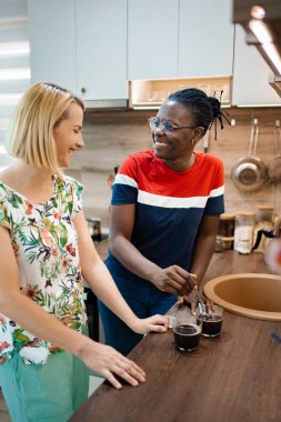 Ilık ve aydınlık bir mutfakta iki arkadaş bir anı neşeyle paylaşıyor. Kahkahalarla dolu samimi bir atmosfer yaratarak birbirlerine gülümserken kahve bardaklarını karıştırırlar..