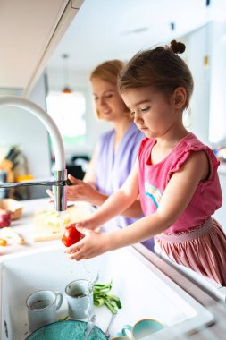 Annesi öğle yemeğini hazırlarken bir kız domates yıkıyor..