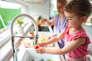 Bir yetişkin yemek hazırlarken çocuk domatesleri duruluyor..