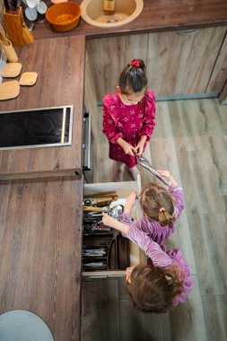 Üç genç kız mutfak keşfi yapıyor, mutfak gereçleriyle dolu bir çekmeceyi karıştırıyorlar. Onların neşeli varlığı sıcacık uzaya sıcaklık katar..