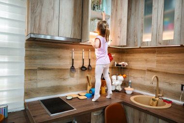 Sıcak, güneşli bir mutfakta, genç bir kız tezgahın üzerinde duruyor, üst raftaki kavanozlara ulaşmak için geriniyor. Etrafını keşfederken, neşeli bir ruh sergileyerek kararlılığı parlıyor..