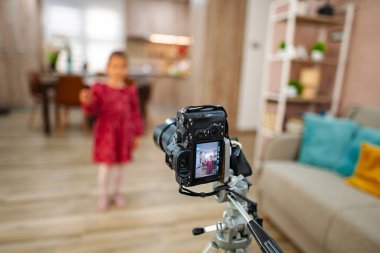 Sıcak, davetkar bir oturma odasında, parlak bir kıyafet giymiş bir çocuk kameraya neşeli bir poz vererek aile fotoğrafçılığında neşeli anılar yaratıyor. Yumuşak ışık anı güçlendirir..