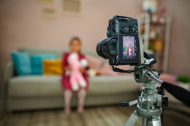 Bir çocuk yumuşak bir kanepede oturur, pelüş bir oyuncağı kucaklarken, bir kamera onların gülümsemesini odanın diğer tarafından yakalar. Yumuşak pastel renkler sıcak bir atmosfer yaratır, anılar için mükemmeldir..