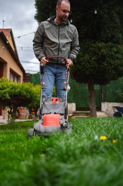 Güneş tepemizde ışıl ışıl parlarken yeşil ve rahat bitkilerle çevrili bahçesindeki çimenleri dikkatlice biçen bir adam, sakin atmosferi güçlendiriyor..