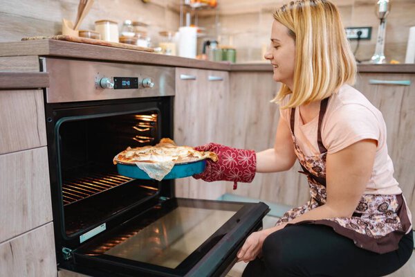 Веселый шеф-повар вытаскивает свежеиспеченный пирог из духовки на своей теплой кухне.