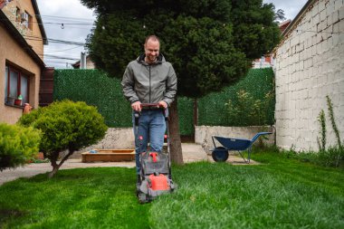 Sakin bir arka bahçede, bir adam canlı yeşil çimleriyle ilgilenmekten zevk alır, çim biçme makinesini kolaylıkla manevra ettirir. Parlak mavi gökyüzü onu çevreleyen yemyeşil alanı tamamlıyor..
