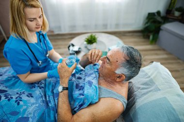 Bakıcı hemşire yaşlı adamın ilaçlarını evde almasına yardım eder..