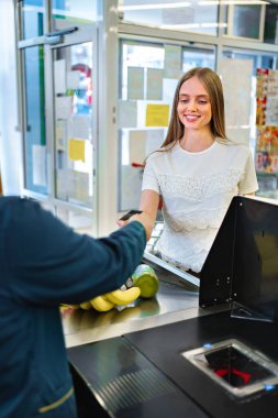 Genç bir kadın güneşli bir öğleden sonra canlı bir marketten taze meyve alırken kasiyerle mutlu bir şekilde etkileşime girer. Neşeli atmosfer onun neşe dolu deneyimini arttırır..