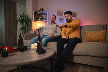 İki arkadaş bir kanepede rahatça oturur, bir film gecesinde nişanlanırlar. Masadaki abur cubur ve içeceklerle kumandada gezinip sıcak, davetkar bir oturma odasında kahkaha ve heyecan paylaşıyorlar..