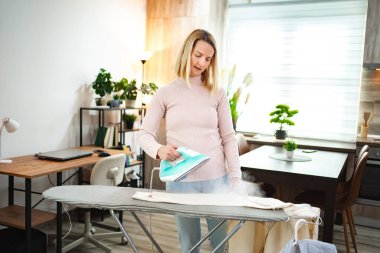 Bir kadın sıcak, aydınlık bir odada temiz çamaşırları dikkatlice ütülüyor..