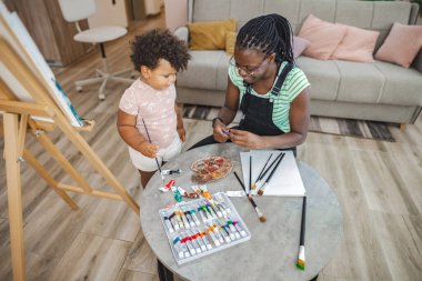 Küçük bir çocuk ve annesi birlikte neşeli bir sanat aktivitesi yapıyorlar..