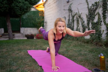 Yeni anne arka bahçesinde yoga yapıyor. İyiliği ve kendine bakımı kucaklıyor..