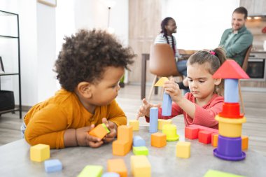 Bir çocuk renkli bloklarla inşa ederken, diğeri dikkatle izliyor..