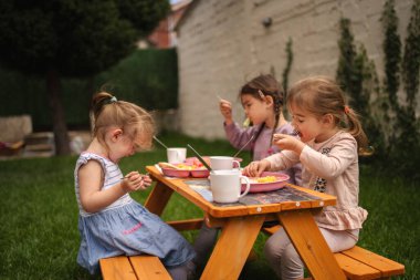 Üç mutlu çocuk sıcak bir günde açık havada renkli yemeklerin tadını çıkarıyor..
