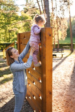 Gülümseyen anne, sevimli kızının oyun parkına çıkmasına yardım ediyor..