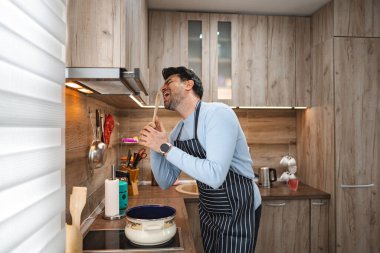 Kahverengi saçlı adam mutfaktaki ahşap sobanın içinde neşeyle şarkı söylüyor..