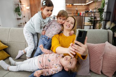 Anne ve üç kızı kanepede oturup evdeki oturma odasında selfie çekiyorlar..