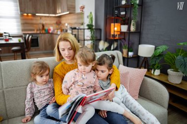 Bir anne ve üç kızı oturma odasında kanepede oturmuş, annelerinin bir hikaye okumasını dikkatle dinliyorlar..