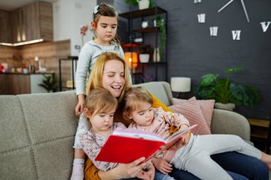 Anne ve üç kızı oturma odasında kanepede oturmuş annelerinin bir hikaye okumasını dikkatle dinliyorlar..