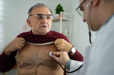 Doktor yaşlı bir adamı muayene ediyor. Klinikte kalp sorunu var mı diye bakıyor..