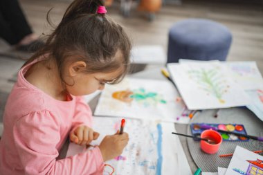 Bir çocuk yaratıcı masasında boya ve boya kalemleriyle resim çizmeye odaklanır..